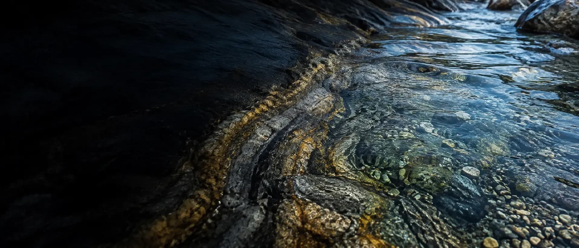 Clear shallow water running over dark mineral-rich rock, pebbles visible beneath the surface.